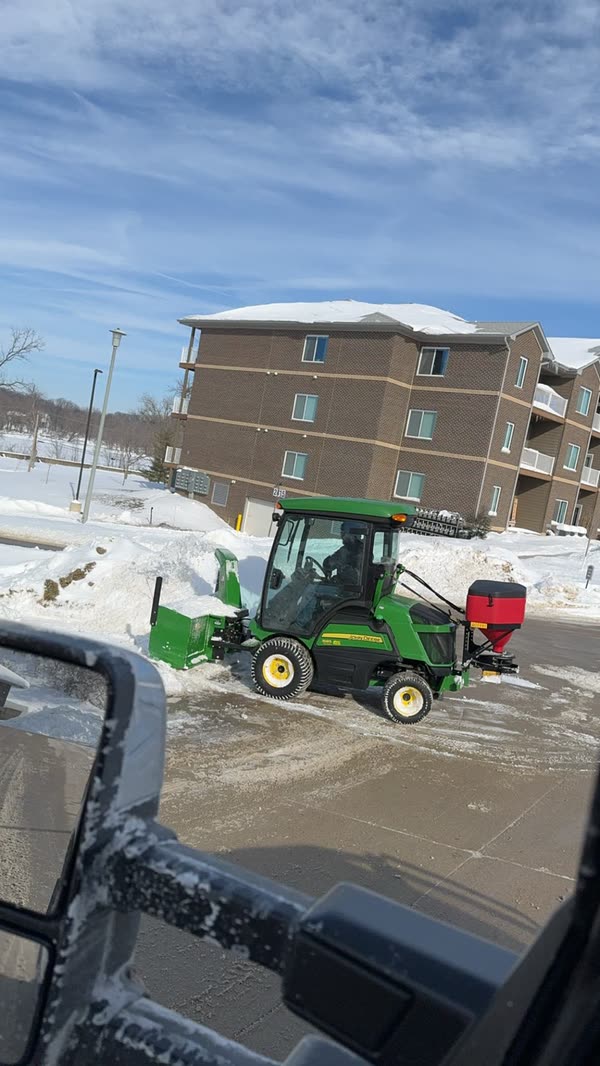 Tractor with a snowblower and spreader clearing an apartment lot