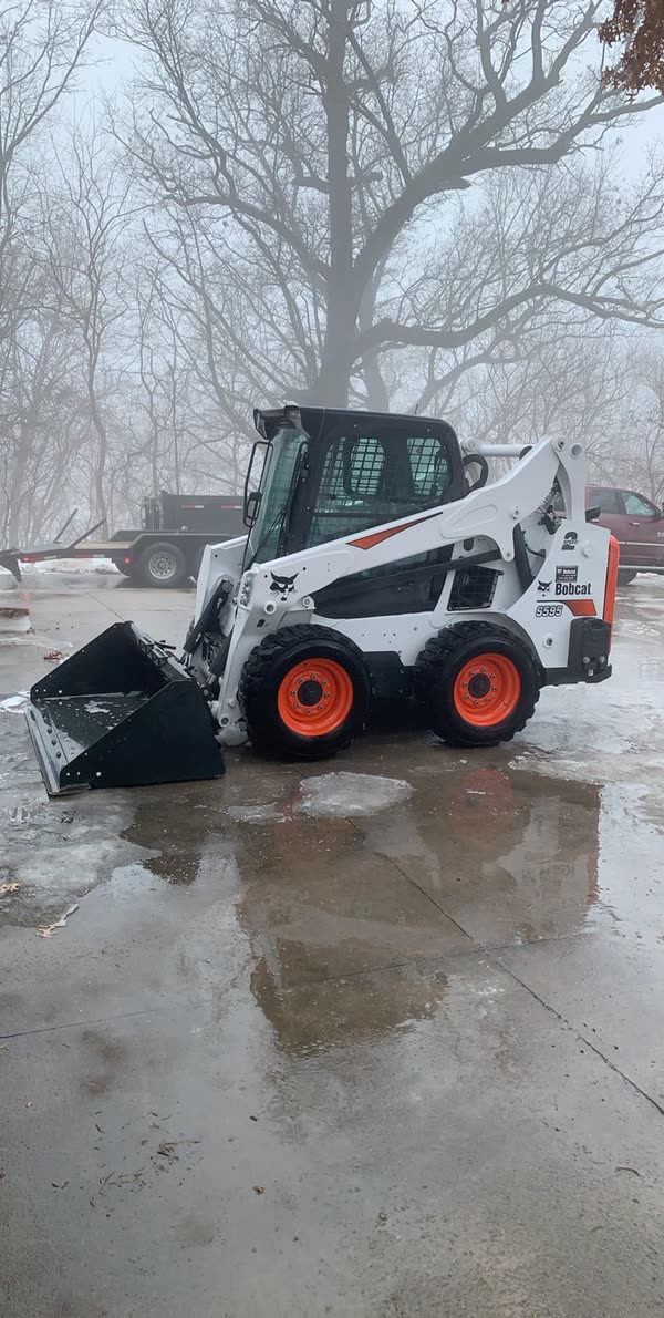 Skid loader staged on a wet lot in winter fog